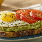 A slice of whole-grain toast topped with mashed avocado, a fried egg, and sliced tomatoes