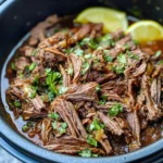 Cooker Barbacoa Beef shredded and juicy in a slow cooker, topped with fresh cilantro and lemon slices.